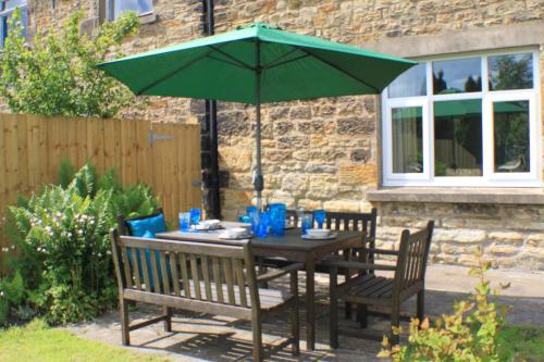a table with a green umbrella and two chairs at Mona's Cottage in Berwick-Upon-Tweed