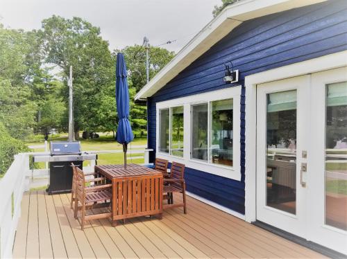 a blue house with a deck with a table and an umbrella at The Ledges Resort & Marina in Alexandria Bay