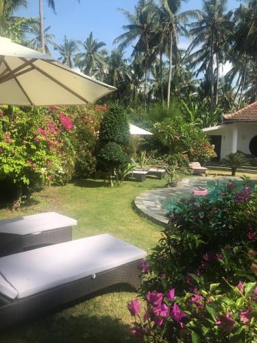 a garden with a table and an umbrella and flowers at Villa Rizki Candidasa in Candidasa