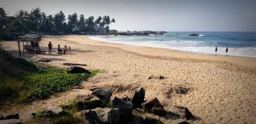 a beach with people standing on the sand and the ocean at Strandvilla Kandu Haus Yin bei Hikka in Dodanduwa