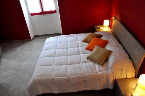 un letto bianco con cuscini arancioni in una camera rossa di S'arenada a Cagliari