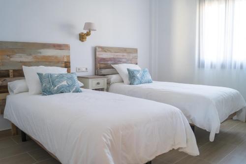2 camas en un dormitorio con sábanas blancas y almohadas azules en Casa de la Jara 10, en Sanlúcar de Barrameda