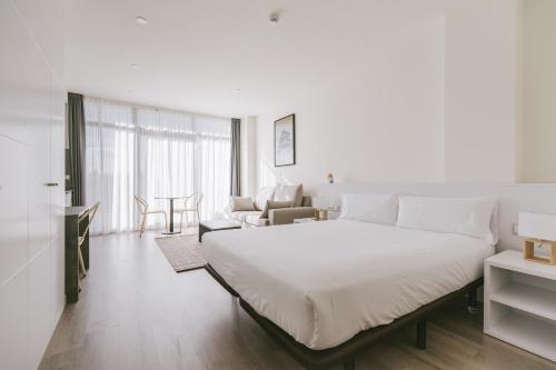 a white bedroom with a large bed and a living room at CIM Aparthotel in Sant Cugat del Vallès