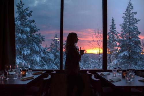 a woman standing in front of a window holding a wine glass at Lapland Hotels Sky Ounasvaara in Rovaniemi