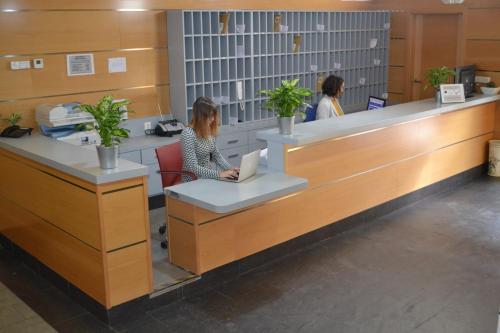 Una donna seduta al bancone in un ufficio con un portatile di The Factory Residence Hall a Segovia