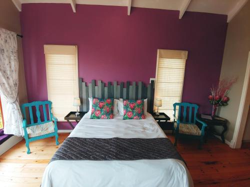 a bedroom with purple walls and a bed with two blue chairs at Happy Homes - Imhoffs Gift in Imhoffʼs Gift