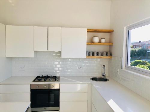 a kitchen with white cabinets and a sink and a window at Seascape in De Kelders