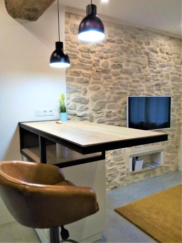 a desk with a chair and a tv on a stone wall at Le Petit Studio - 15 m2 - Centre Ville - Sorgue à 50 m in LʼIsle-sur-la-Sorgue