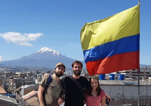 a group of three people standing next to a rainbow flag at La Merced Plaza Hospedaje in Riobamba