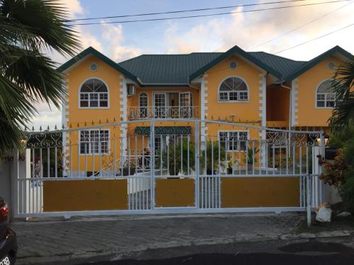 a yellow house with a white fence at Faith's Villa Tobago in Diamond