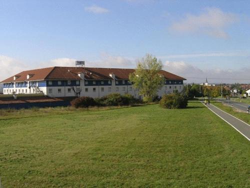 a large white building with a grassy field next to a road at Center Hotel Drive Inn in Hirschaid