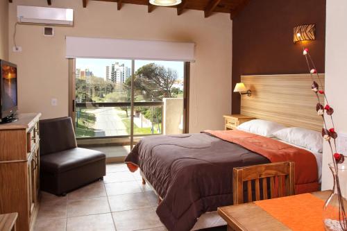 un dormitorio con una cama y una silla y una ventana en el Alpemar Apart Hotel & Spa en Villa Gesell