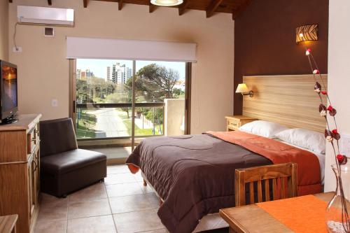 een slaapkamer met een bed, een stoel en een raam bij Alpemar Apart Hotel & Spa in Villa Gesell