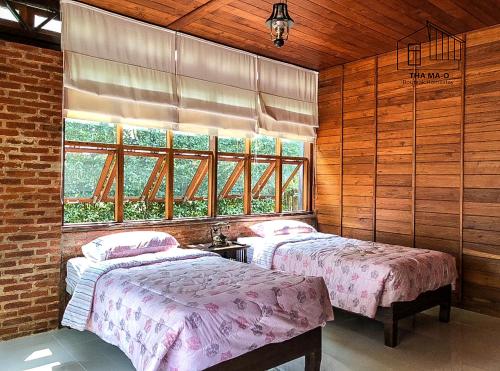 Duas camas num quarto com paredes e janelas de madeira em ท่ามะโอบูทีคโฮมสเตย์ Tha Ma-O Bouteak Homestay em Lampang