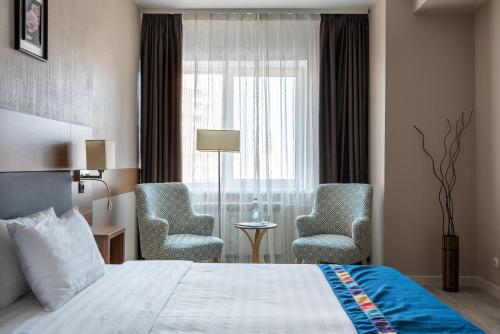 ウラジオストクにあるアストリア ホテルのベッド1台、椅子2脚、窓が備わる客室です。