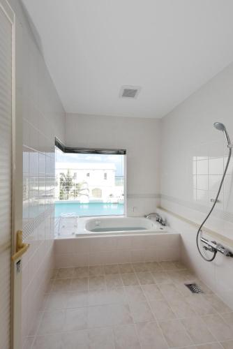 a white bathroom with a tub and a window at Route 6 Inn in Yomitan