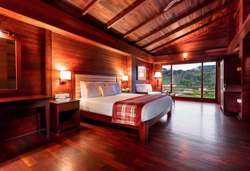 ein Schlafzimmer mit einem Bett und einem großen Fenster in der Unterkunft GReaT trails Kodaikanal by GRT Hotels in Kodaikanal