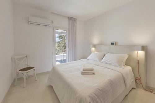 a white bedroom with a large white bed and a chair at Apartment with a sea view and swimming pool, in the area of Koundouros in Koundouros