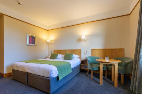 タラモアにあるTullamore Court Hotelのベッド、テーブル、椅子が備わるホテルルームです。