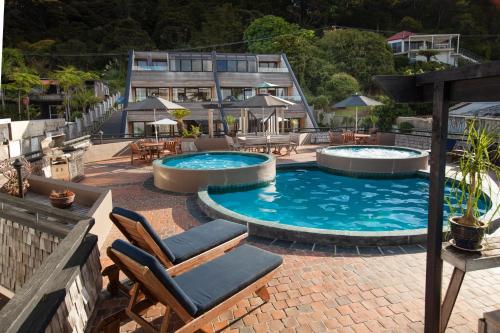 a swimming pool with two chairs and a house at Pioneer Waterfront Apartments in Paihia