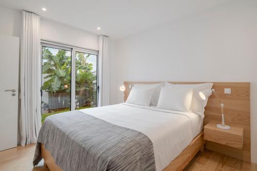 a bedroom with a white bed and a large window at Casas da Vargem shared swimming pool by An Island Apart in Ponta do Sol