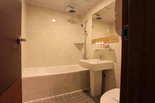 a bathroom with a tub and a sink and a toilet at Hotel W Topdong in Jeju