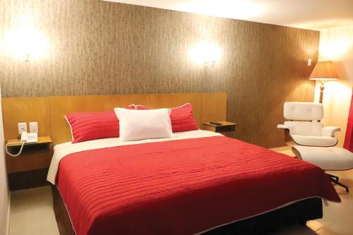 um quarto com uma cama vermelha e uma cadeira branca em Royal Madero Inn em Ciudad Madero