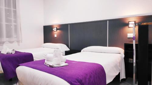 two beds in a hotel room with purple sheets at Hostal Doña Isabel in Majadahonda