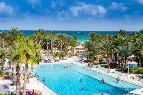 a pool at a resort with palm trees and the ocean at Palm Beach Club Djerba - All Inclusive in Midoun