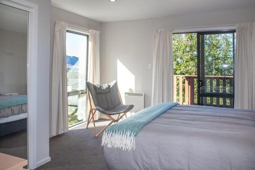 a bedroom with a bed and a chair and a balcony at Treetop Lodge - Acheron Holiday Home in Hanmer Springs