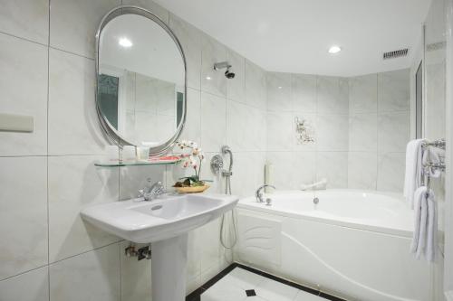 a white bathroom with a sink and a tub and a mirror at Charming Castle Hotel in Taipei