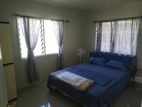 a bedroom with a blue bed and two windows at Kuinis Guesthouse in Apia