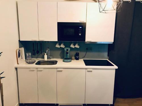 a kitchen with white cabinets and a sink and a microwave at Petit studio cosy in Bobigny