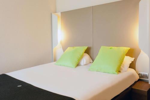 a white bed with two lime green pillows on it at Campanile Angers Ouest - Beaucouzé in Beaucouzé