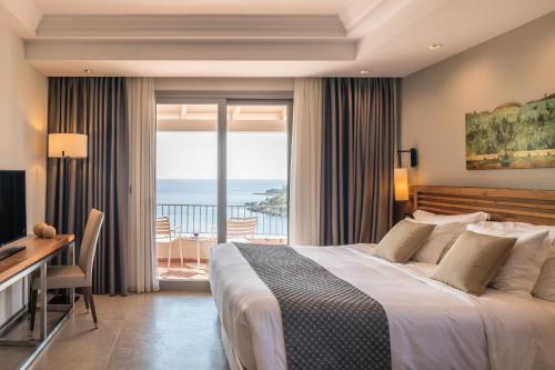 a bedroom with a bed and a desk and a balcony at Domotel Agios Nikolaos Suites Resort in Syvota