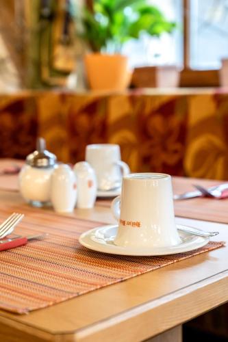 a table with a white coffee cup on a plate at Hotel Hölzer Bräu by Lehmann Hotels in Ebersberg