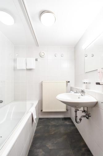 a white bathroom with a sink and a bath tub at Hotel Hölzer Bräu by Lehmann Hotels in Ebersberg