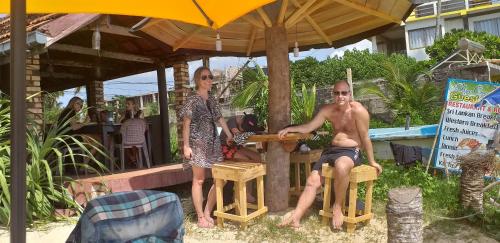a man and a woman sitting at a table under an umbrella at Blue Corals Beach Bungalow in Madihe East