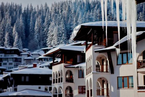 a building with snow on the roof of a town at GRAND MONASTERY Apartments in Pamporovo