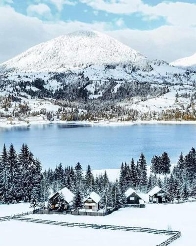 a snow covered mountain with houses and a lake at Aqualina Colibita - pe malul lacului in Colibiţa