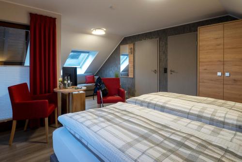 a hotel room with a bed and two red chairs at Restaurant - Pension Im Pfenn in Irrhausen