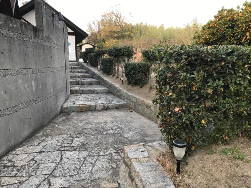 a stone path next to a wall with an orange hedge at Shiraishi Island International Villa in Kasaoka