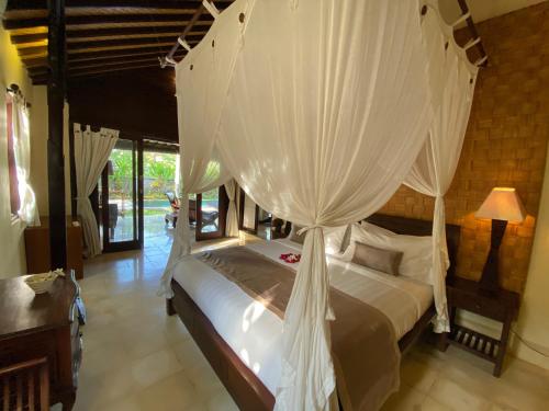 a bedroom with a canopy bed with white drapes at Rumah Dadong in Ubud
