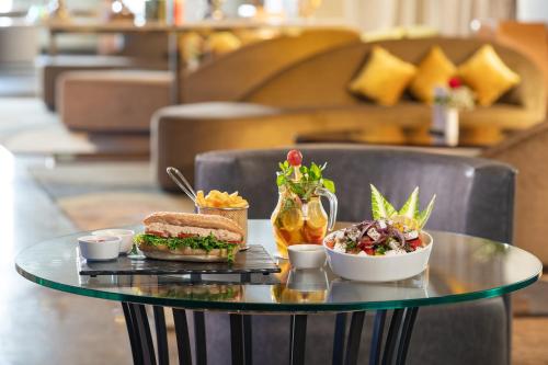 a glass table with a sandwich and salad on it at Millennium Makkah Al Naseem in Makkah