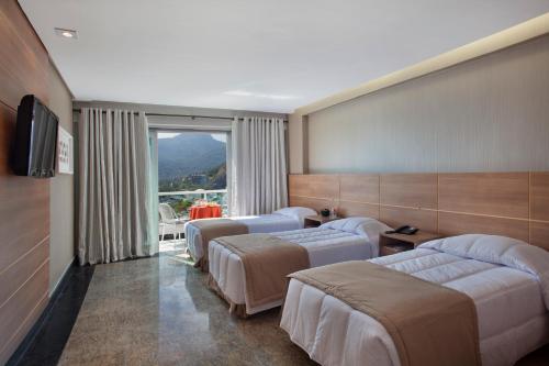 a hotel room with three beds and a window at Royalty Barra Hotel in Rio de Janeiro