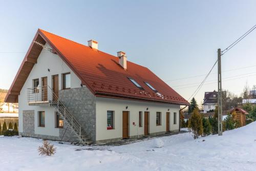 a house with an orange roof in the snow at Apartamenty pod Gromadzyniem in Ustrzyki Dolne