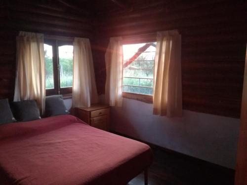 1 Schlafzimmer mit einem roten Bett und 2 Fenstern in der Unterkunft Cabañas Buen Ayre in Villa Rumipal