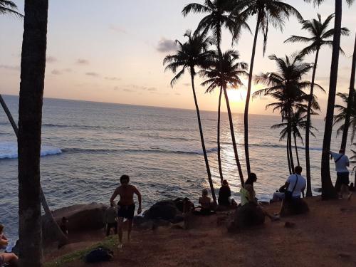 a group of people sitting on the beach watching the sunset at Edelweiss Resort in Mirissa