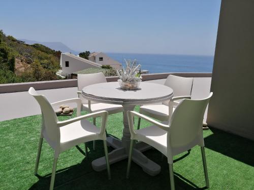 a white table and chairs on a balcony with the ocean at Froggy at the Pond in Simonʼs Town