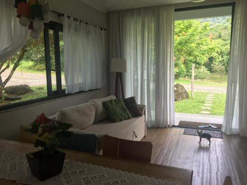 a living room with a couch and a large window at Refúgio da família - serra & lago in Guapimirim